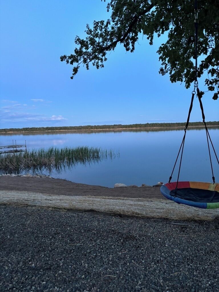 Una silla colgante junto a un lago tranquilo con cielo despejado.