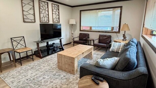 A living room with a sofa, coffee table, TV, and a window with blinds. - Quiet retreat on Little Whitefish Lake (Garrison)