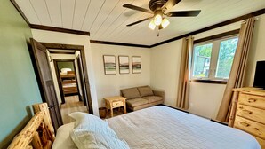 A bedroom with a bed, a wooden dresser, a nightstand, a ceiling fan, and a window with curtains. - Quiet retreat on Little Whitefish Lake (Garrison)