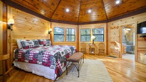Un dormitorio rústico de madera con una cama grande, un banco de madera, un escritorio y un televisor.