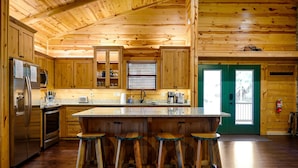 Cocina de cabaña de madera con una isla central, taburetes de bar y una puerta verde.