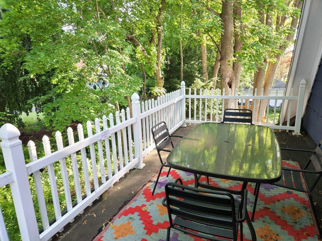Une terrasse couverte, agrémentée d’une clôture en bois peinte en blanc, d’une table et de chaises.