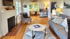 A spacious living room with a fireplace, a sofa, a coffee table, and a dining area. - Vacation Starts Now! Pet friendly, beach fun 5 min away! (New London)