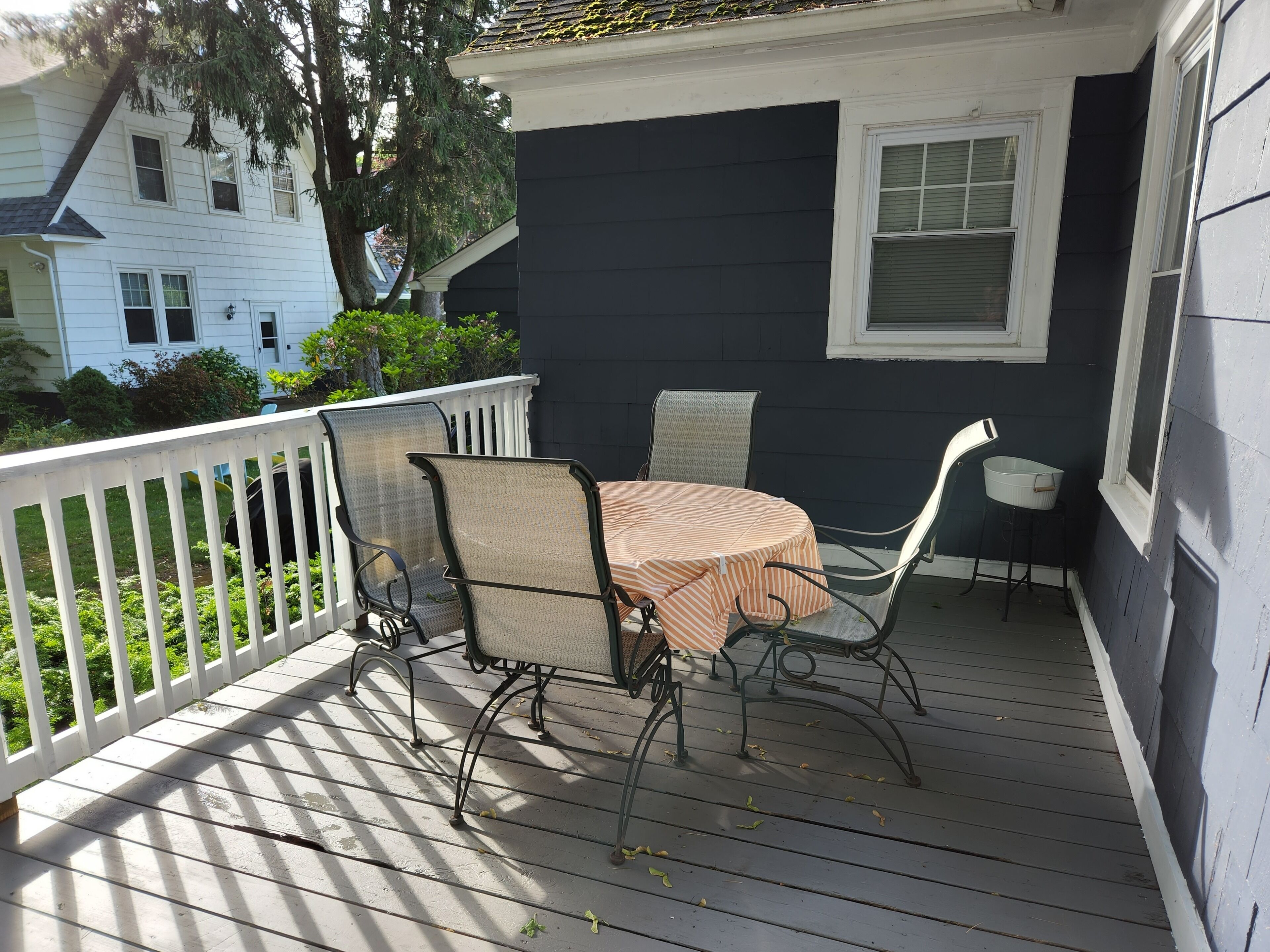 Une terrasse couverte avec une table et des chaises, une rambarde blanche et une fenêtre.