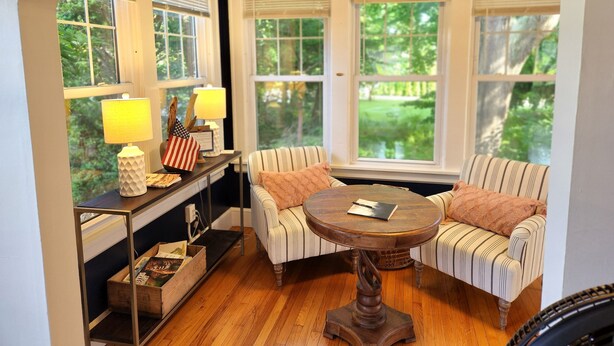 A cozy room with a wooden floor, a round table with a book, striped sofas, and a small side table with lamps and decorative items. - Vacation Starts Now! Pet friendly, beach fun 5 min away! (New London)