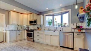 A modern kitchen with white cabinetry, a central island, stainless steel appliances, and a window providing natural light. - Vacation Starts Now! Pet friendly, beach fun 5 min away! (New London)