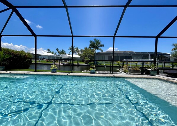 Une piscine aux eaux cristallines, avec vue sur une maison et des palmiers en arrière-plan.