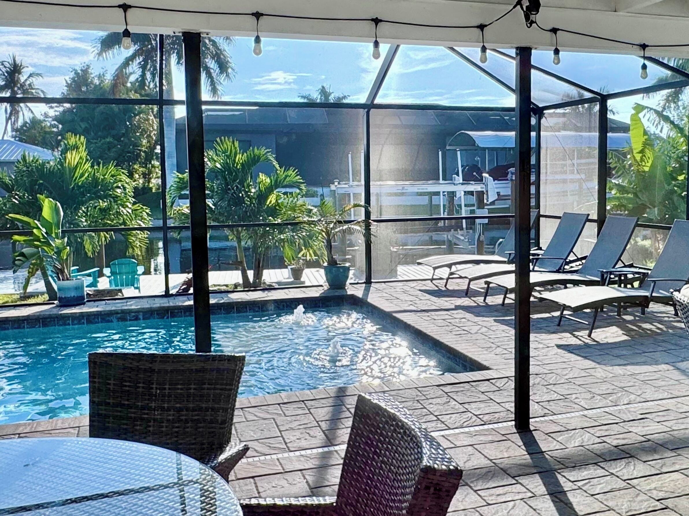 A pool area with lounge chairs and a table, surrounded by potted plants and a clear view of the sky.