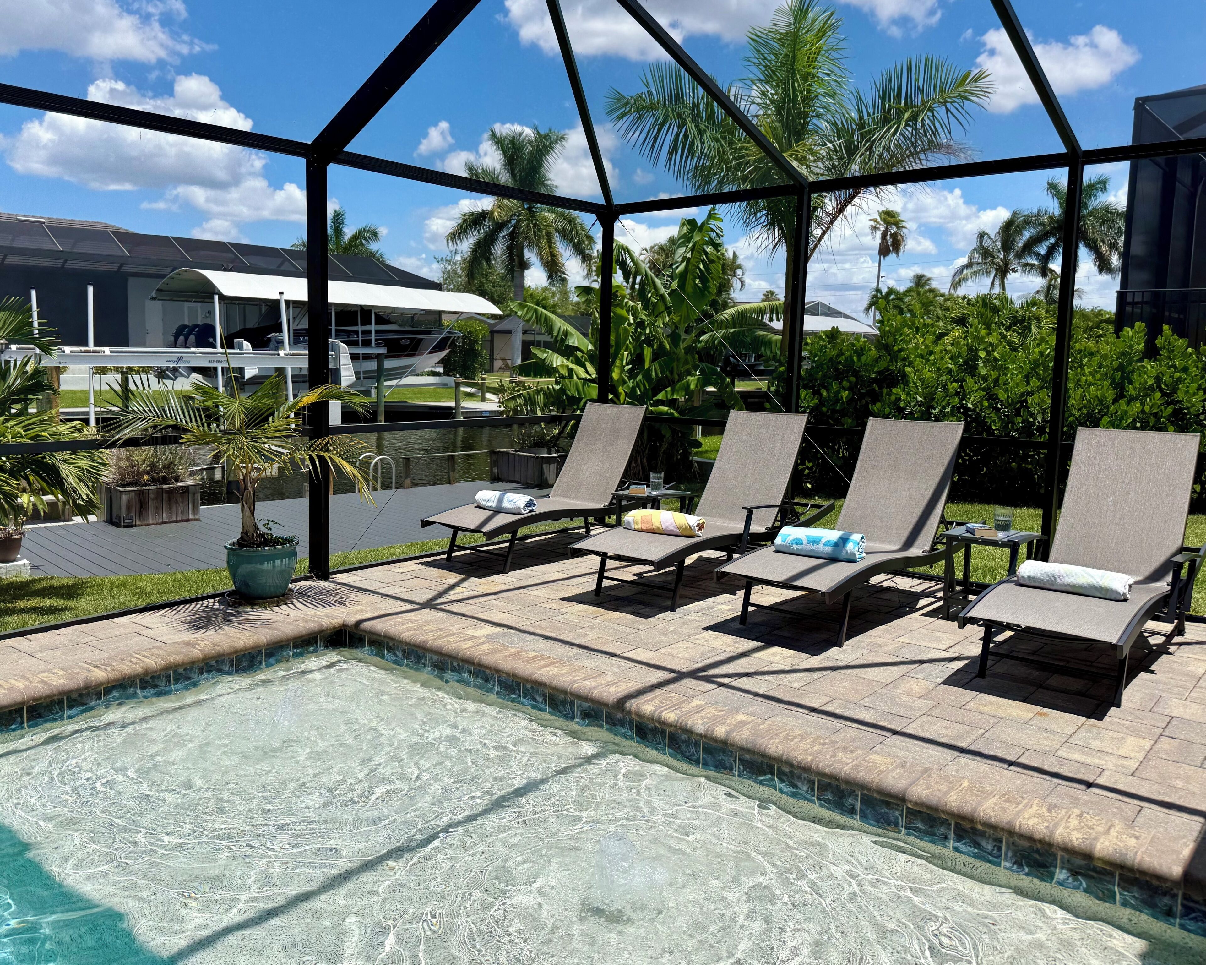 Zona junto a la piscina con sillas de descanso y vistas a una casa y palmeras.