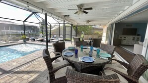Eine Terrasse im Freien mit Pool, Korbmöbeln und einem Tisch, der zum Essen gedeckt ist.