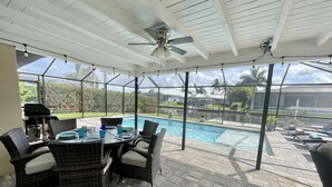 Ein überdachter Patio-Bereich mit Pool, Korbmöbeln und Deckenventilator.