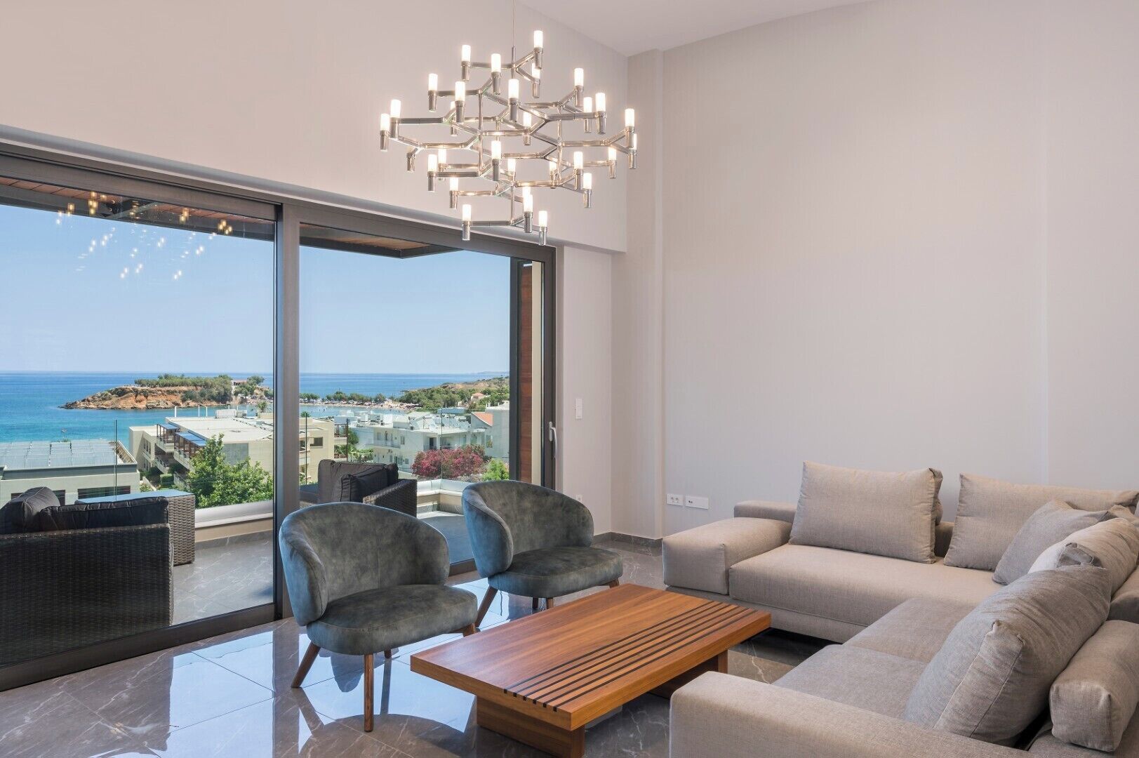 A modern living room with a view of the sea, a chandelier, and a sofa.