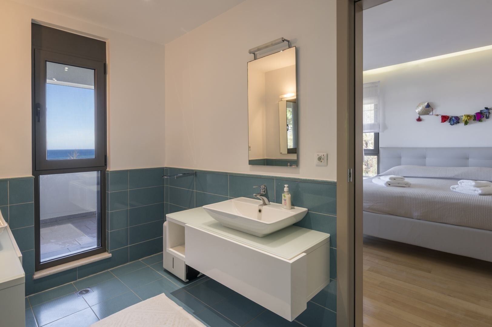 Un bany modern amb una finestra gran, un lavabo blanc i un mirall.
