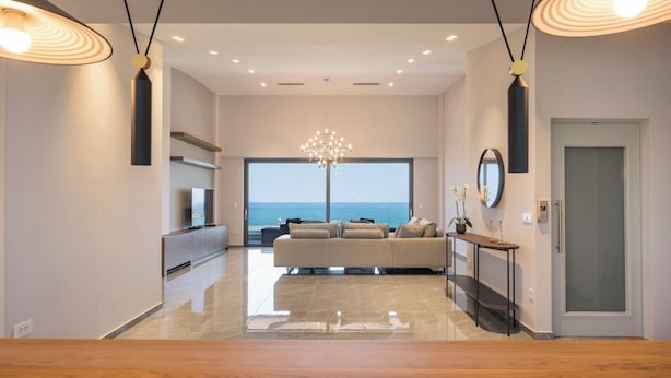 Een ruime woonkamer met een groot raam met uitzicht op zee, een moderne kroonluchter en een minimalistisch design.