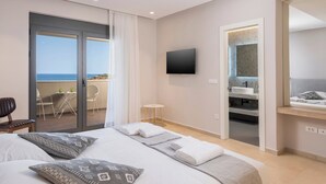 Een moderne hotelkamer met een groot bed, een balkon met uitzicht op zee, een aan de muur bevestigde televisie, en een badkamer met spiegel en wastafel.