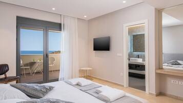 A modern hotel room with a large bed, a balcony with a view of the sea, a TV mounted on the wall, and a bathroom with a mirror and sink.
