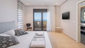 Een moderne hotelkamer met een bed, een televisie, een balkon met uitzicht op zee en een kleine tafel met stoelen.