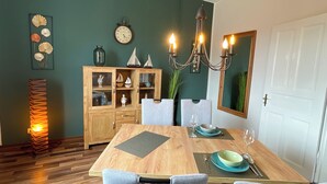A dining area with a wooden table, grey upholstered chairs, a chandelier, a clock, and a cabinet with decorative items.