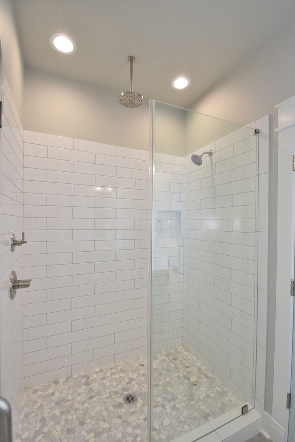 A glass-enclosed shower with white tiled walls and a pebble-patterned floor.