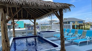 A pool area with a thatched roof structure, lounge chairs, and a pool.