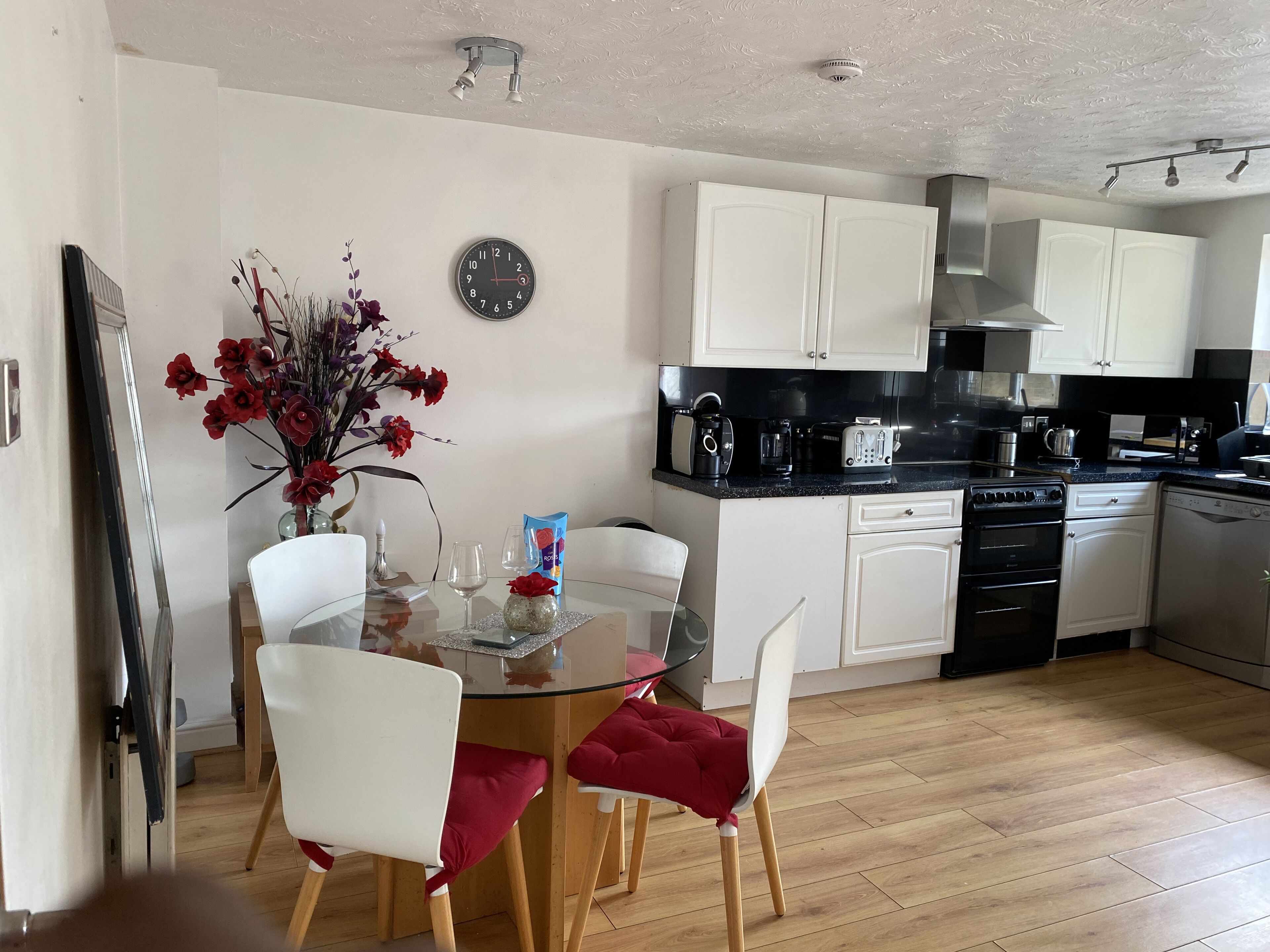 A modern kitchen with white cabinets, a black countertop, and a dining area with a glass table and red chairs.