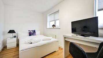 A bedroom with a bed, a desk, a television, a chair, a nightstand, a lamp, and a window.