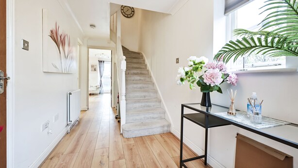 A hallway with a staircase, a radiator, and a vase with flowers on a console table. - Riverside Townhouse with private Garden (London)