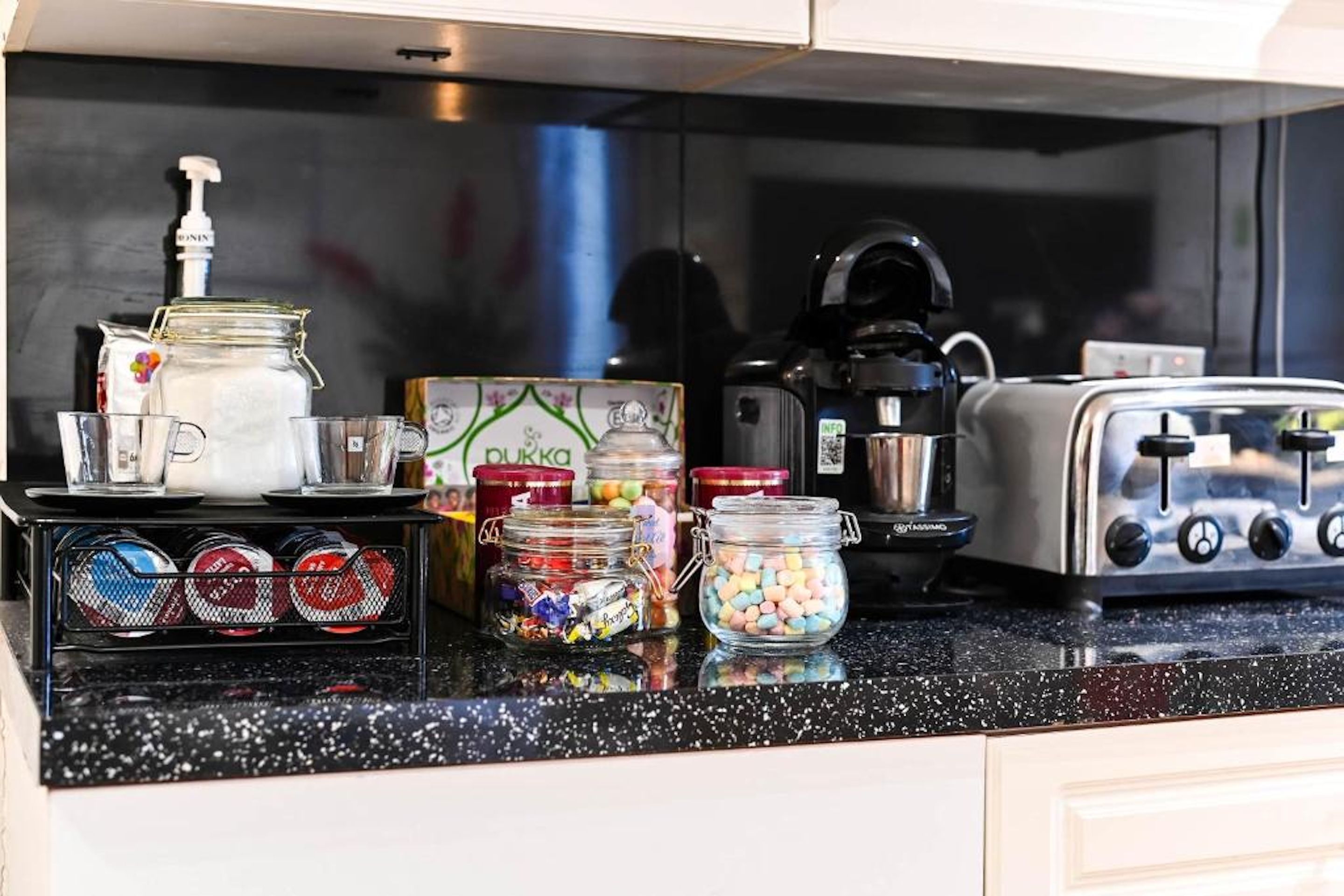 A kitchen counter with various items including a coffee maker, a toaster, jars, and a bag of sugar.