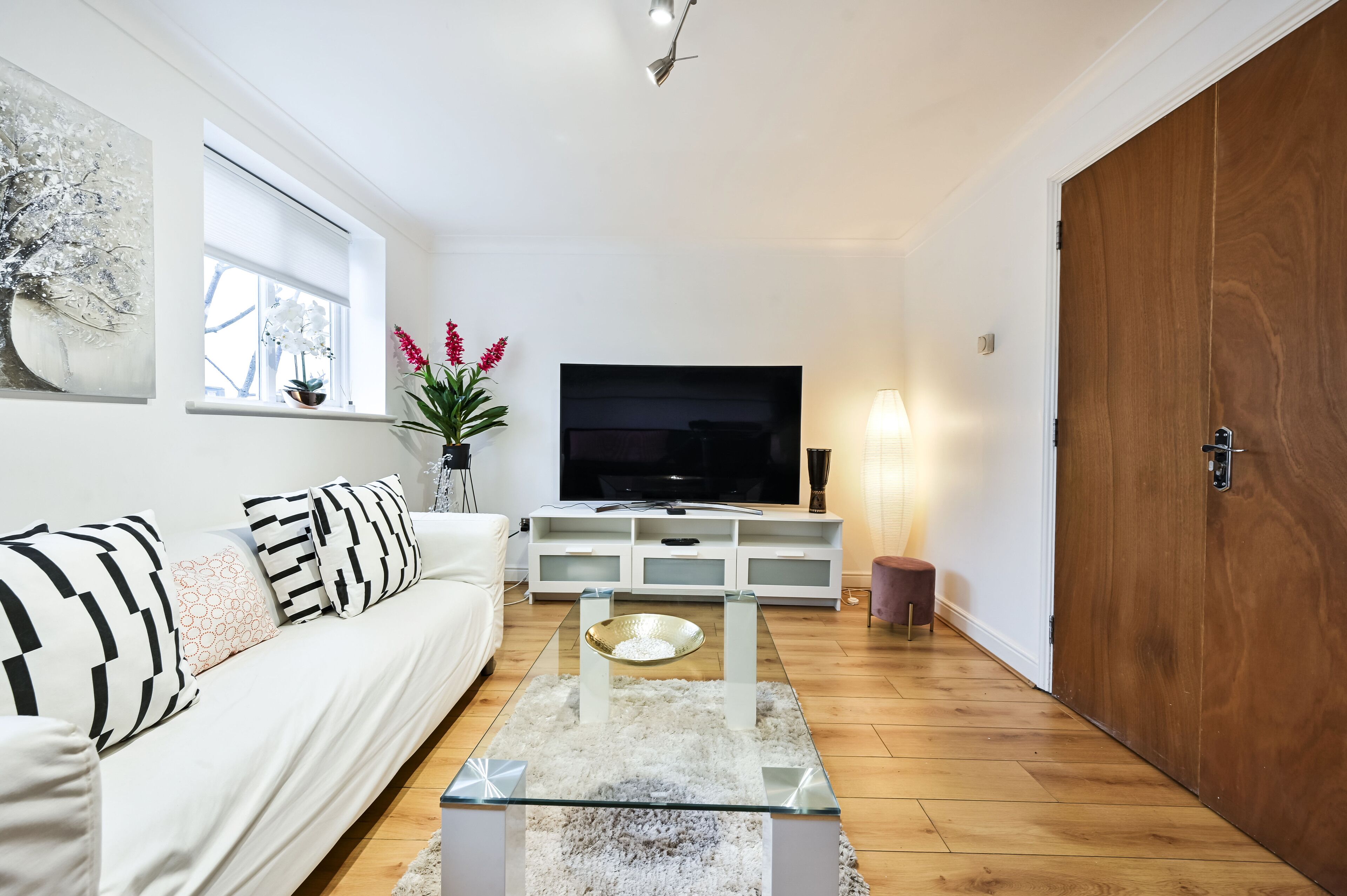 Una sala de estar moderna con un sofá blanco, una mesa de centro de vidrio, un televisor de pantalla plana y una puerta de madera.