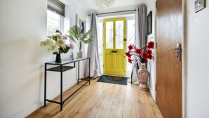 A hallway with a wooden floor, a black metal console table with a vase of flowers, a yellow door, and a white wall. - Riverside Townhouse with private Garden (London)