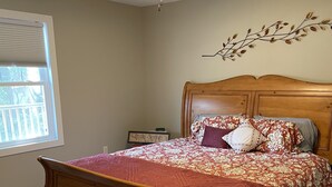 Quarto com cama de madeira, ventoinha no teto, janela com persianas e um adorno na parede.