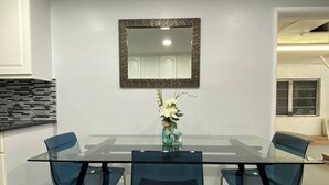 Uma sala de jantar moderna com mesa de vidro e cadeiras azuis, um vaso decorativo com flores e um espelho na parede.