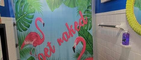 A bathroom with a blue wall, a shower curtain with flamingos and tropical leaves, a toilet, a sink, and a mirror.