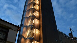 A tall building with a unique facade featuring vertical slats and a series of illuminated windows. - FL Hotel Asakusa (Tokyo)