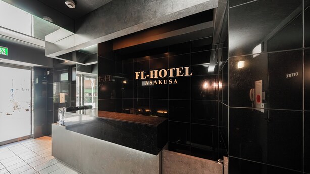 A reception desk with 'FL-HOTEL ASAKUSA' signage, a modern interior with black and grey tiles, and a visible emergency exit sign. - FL Hotel Asakusa (Tokyo)