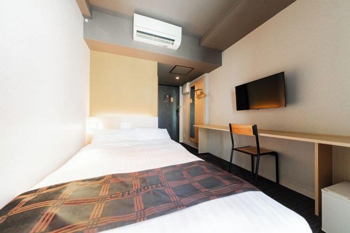 A hotel room with a bed, a desk, a chair, a television, and an air conditioning unit.