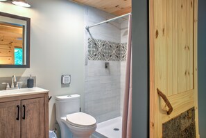 Une salle de bain avec un meuble-lavabo en bois, des toilettes, une douche avec un mur recouvert de carreaux à motifs et une porte en bois.