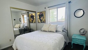 A bedroom with a large bed, a mirror, artwork on the wall, a window with curtains, and a small teal nightstand. - Archie's Place: 20 minute's from the Great Sand Dunes (Blanca)