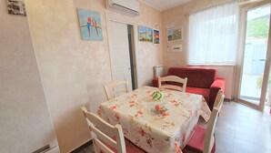 A dining area with a table covered in a floral tablecloth, surrounded by wooden chairs with red cushions. There is a red sofa against the wall and a window with curtains. - Tropea, Appartamenti Borgo Panoramico N .10 (Tropea)