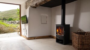 A room with a wood-burning stove, a television mounted on the wall, and a wicker basket. - Snowdonia Cottage with Stunning views of Bala lake and mountains (Llangower)