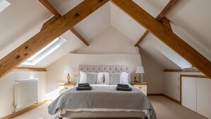 A bedroom with a sloped ceiling, exposed wooden beams, a bed with a grey quilt, two bedside tables with lamps, and a radiator. - Snowdonia Cottage with Stunning views of Bala lake and mountains (Llangower)