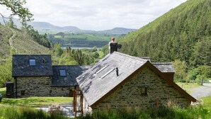 A stone house with a sloped roof, a small attached structure, and a view of a valley and mountains in the background. - Snowdonia Cottage with Stunning views of Bala lake and mountains (Llangower)