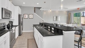 A modern kitchen with white cabinetry, stainless steel appliances, and a black countertop island. - Beautiful TownHome With Pool Near Disney! (Kissimmee)