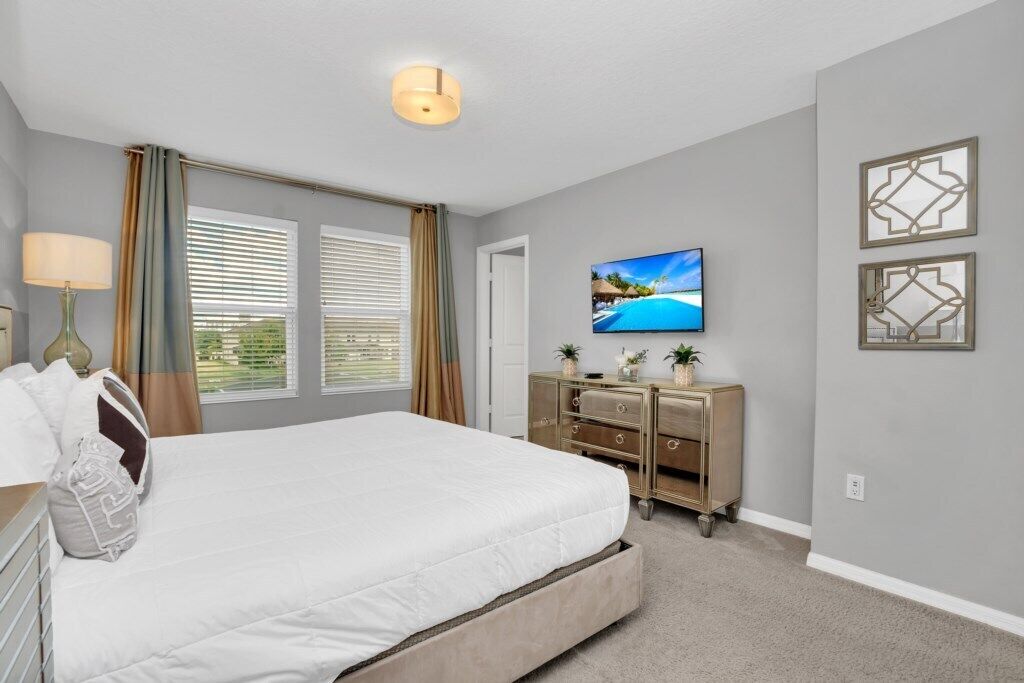 A bedroom with a bed, a dresser, a TV, and a window with curtains.