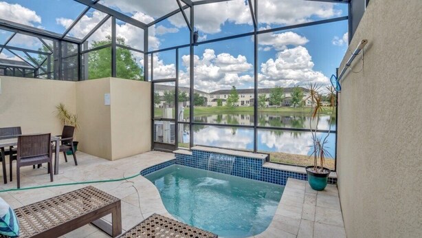 A covered outdoor pool area with a view of a lake, a patio with furniture, and a potted plant. - Beautiful TownHome With Pool Near Disney! (Kissimmee)