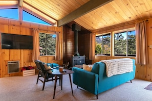 Un intérieur de chalet chaleureux avec des murs en bois, une grande fenêtre, une cheminée et un téléviseur.