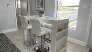A modern kitchen with a white island, bar stools, and a window with blinds. - Welcome to this stylish and spacious luxury suite (Fort Lauderdale)