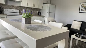 A modern kitchen with white cabinetry, a central island with a plant, and a dining area with white chairs. - Welcome to this stylish and spacious luxury suite (Fort Lauderdale)