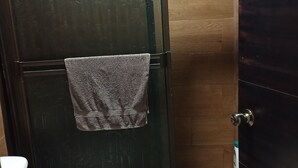 Ein Badezimmer mit Duschabtrennung aus Glas, einem Handtuch, das an der Tür hängt, einer Toilette und Holzboden.