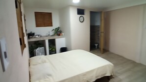 Ein Schlafzimmer mit einem Bett, einem kleinen Schreibtisch mit Pflanze, einer Wanduhr und einer Tür zu einem anderen Raum.